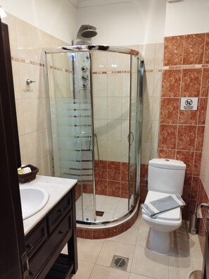 A bathroom with a glass-enclosed shower, a white toilet, and a vanity with a sink and drawers.