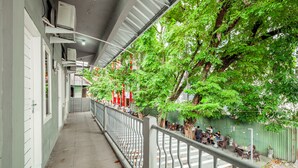 A corridor with a railing, trees, and outdoor seating area. - Hotel O Wongso Residence Syariah (Pangkalpinang)