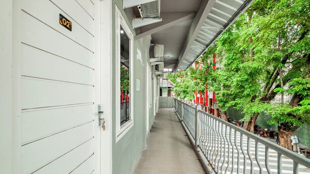 A corridor with a metal railing, a door with a number sign, and a view of greenery outside. - Hotel O Wongso Residence Syariah (Pangkalpinang)