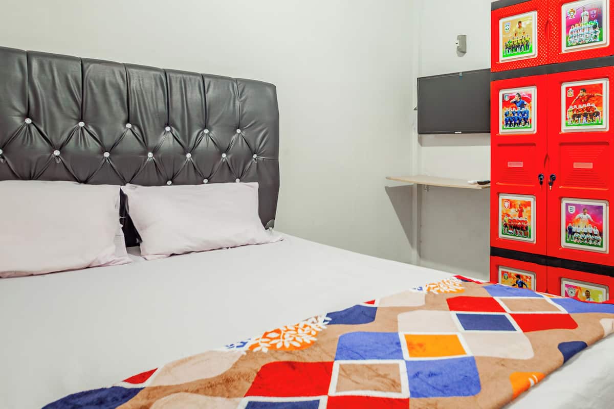 Una cama con cabecera capitonada, dos almohadas y una colcha colorida.