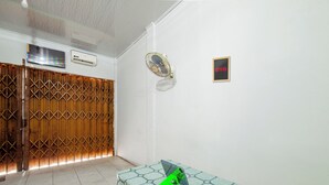 A room with a tiled floor, a wooden partition, a table with a green object, a wall-mounted fan, and a TV. - Hotel O Wongso Residence Syariah (Pangkalpinang)