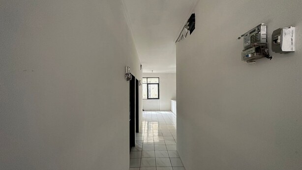Un pasillo estrecho con paredes blancas y suelo de baldosas que conduce a una habitación con ventana.