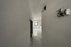 A narrow hallway with white walls and tiled flooring leading to a room with a window.