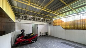 Un área de estacionamiento techada con una motocicleta roja, unidades de aire acondicionado y una pared de ladrillo.