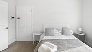 A minimalist bedroom with a large bed, two bedside tables, and a door. - TTSA - Essential 1 Bedroom Apartment 2 - Croydon (Croydon)