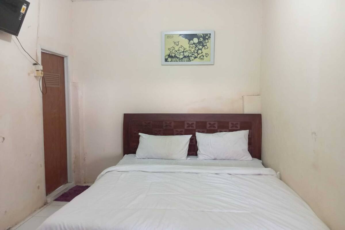 A small, clean room with a single bed, a wooden headboard, a wall-mounted TV, and a door.