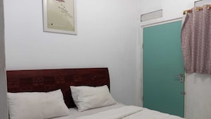 A bedroom with a wooden headboard, two white pillows, a teal door, and a curtain.