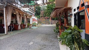 A covered outdoor area with a gravel path, potted plants, and a sign with text.