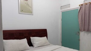 A bedroom with a wooden headboard, two pillows, a bed with a white bedspread, a teal door, and a curtain. - OYO 93631 Eltsania Exclusive Homestay Syariah (Bandar Lampung)