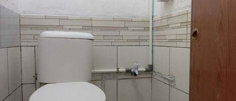 A small, tiled bathroom with a toilet, a hand dryer, and a wall-mounted soap dispenser.