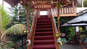 A wooden staircase with a 'WELCOME' sign at the top, leading to a covered area with outdoor seating and potted plants. - OYO 93631 Eltsania Exclusive Homestay Syariah (Bandar Lampung)