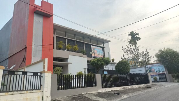 A modern building with a red and white facade, multiple balconies, and a gated entrance. - Hotel O Rumah Singgah Cemara Syariah (Pekanbaru)