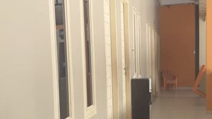 A hallway with doors leading to rooms, a trash bin, and a chair in the distance. - Hotel O Rumah Singgah Cemara Syariah (Pekanbaru)