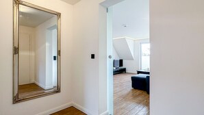 Ein Flur mit einem großen Spiegel, einer Tür zu einem Wohnbereich mit Fernseher und einem Holzboden.