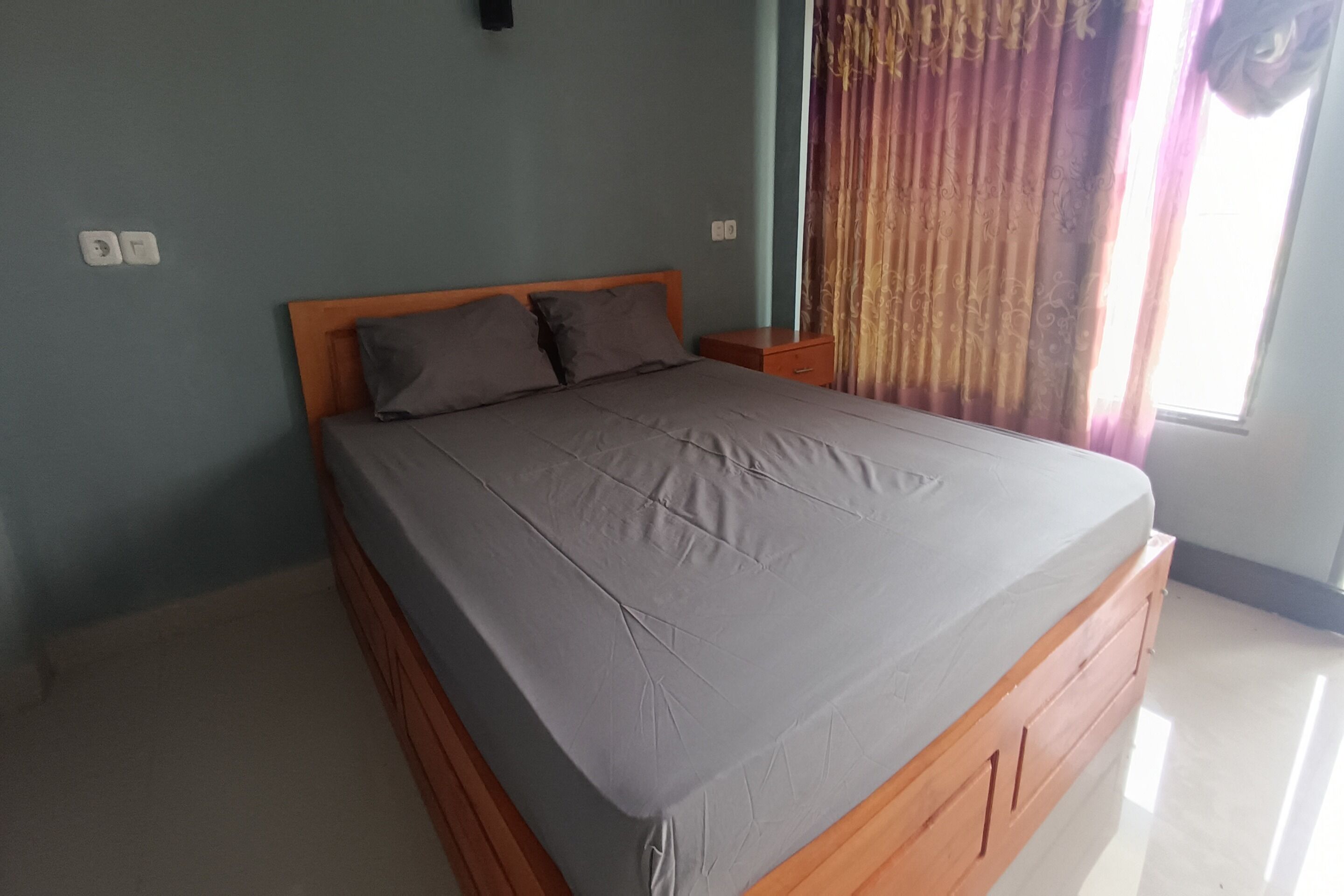 Een slaapkamer met een eenpersoonsbed, een nachtkastje en een raam met gordijnen.