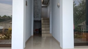 Un couloir étroit avec un escalier menant à l’étage supérieur. Les murs sont unis et blancs, et il n’y a aucun meuble ni élément de décoration visible.