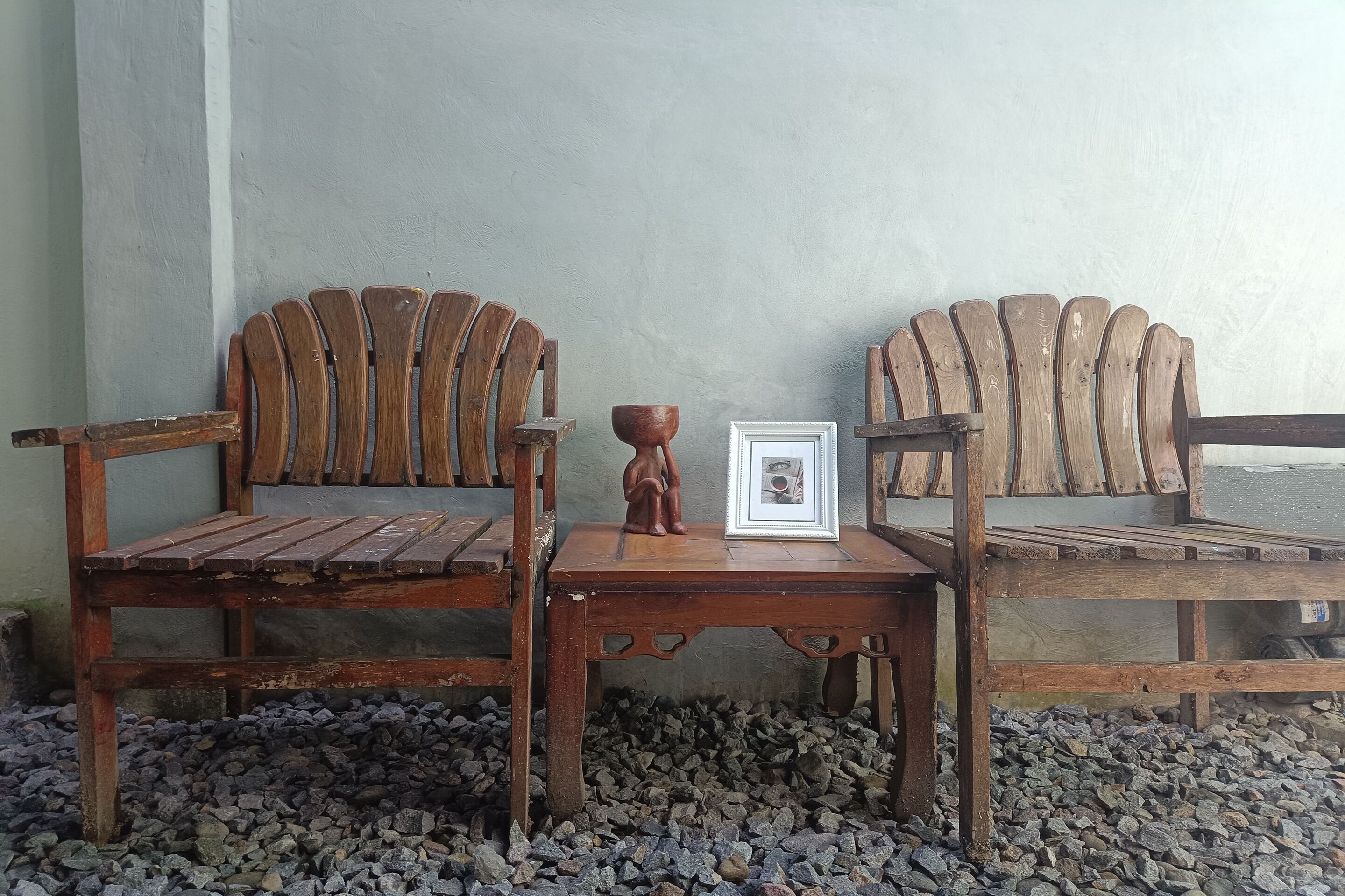 Two wooden chairs with curved backs and a small table with a picture frame and a bowl between them.