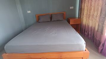 A single bed with a wooden headboard and a grey mattress in a room with light blue walls.