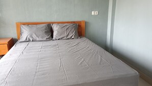 Un lit avec une tête de lit en bois et deux oreillers, une table de chevet à gauche et un interrupteur sur le mur.