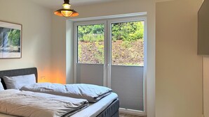 Une chambre à coucher avec un lit, une fenêtre avec des stores, un luminaire suspendu et un radiateur.