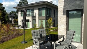 Une terrasse extérieure moderne avec une table en verre et quatre chaises grises dotées de coussins.