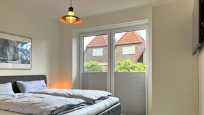 Ein Schlafzimmer mit einem Bett, einer Hängelampe, einem Fenster mit Jalousien und einem Bild an der Wand.