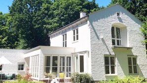 Een tweelaags huis met een stenen gevel, een overdekte veranda met stoelen en een verzorgde tuin.