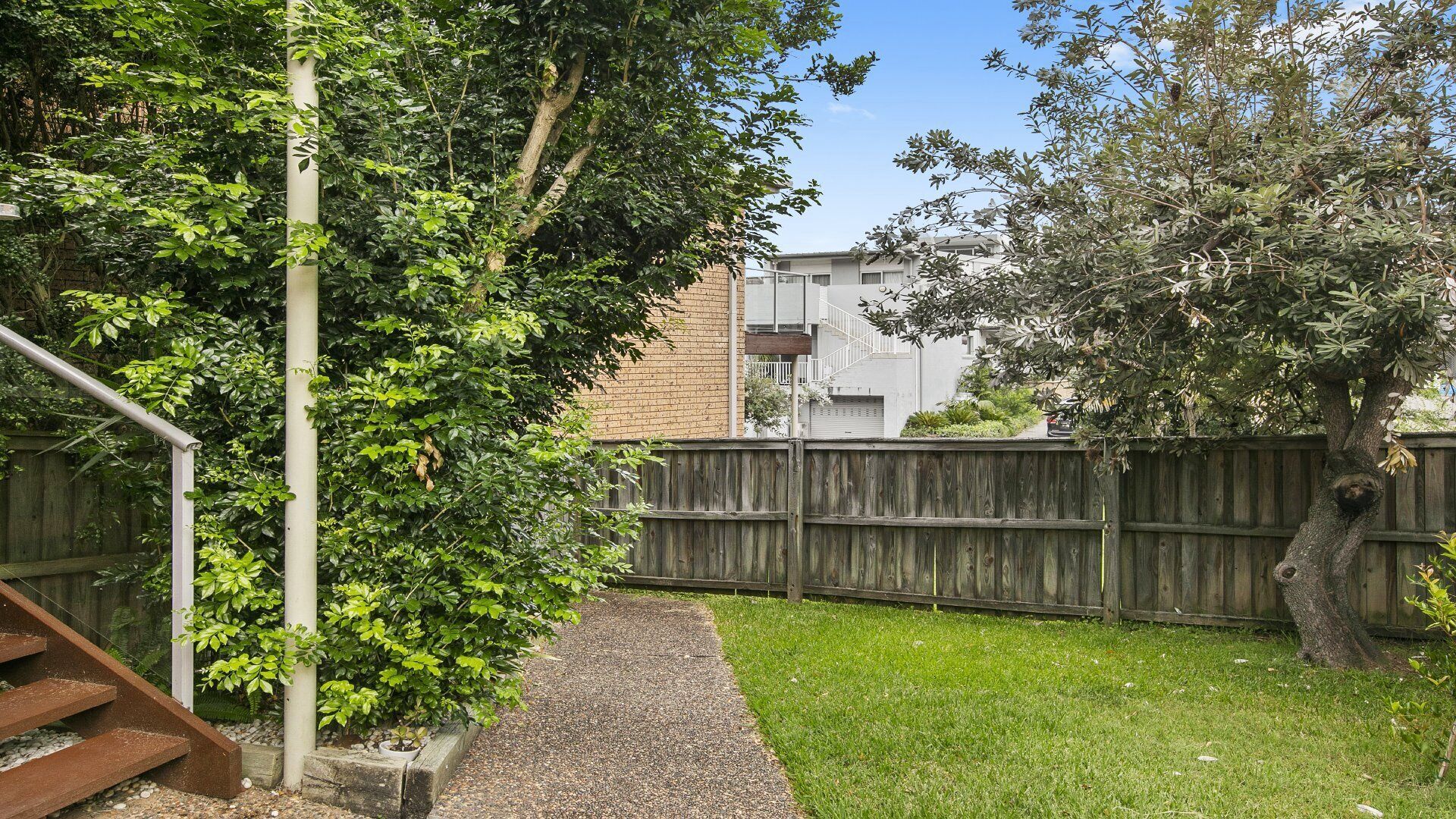 A backyard with a wooden fence, a gravel path, and a grassy area.