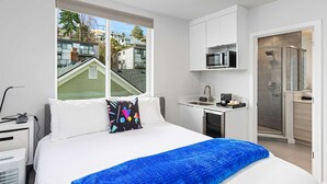 A modern hotel room with a large bed, a desk with a microwave, and a shower area. - The Futuristic Hoverboard Sweet Suite (Seattle)