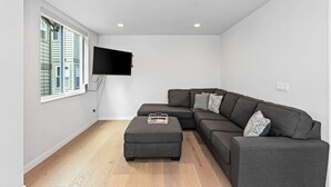 A modern living room with a sectional sofa, a flat-screen TV mounted on the wall, and a wooden floor. - The Futuristic Hoverboard Sweet Suite (Seattle)