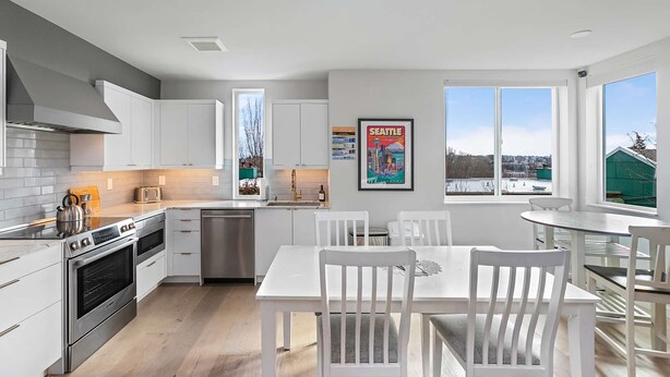 A modern kitchen with white cabinets, stainless steel appliances, and a large window offering a view of the city. - The Futuristic Hoverboard Sweet Suite (Seattle)