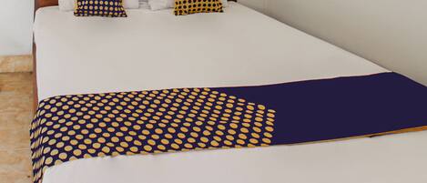 A bed with a white mattress, two pillows with geometric patterns, and a dark blue blanket with yellow dots.