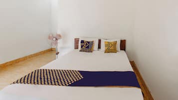 Una cama con colchón blanco, manta de diseño azul y amarillo, y dos almohadas con motivos azules y amarillos.