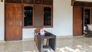 A room with two wooden doors, a window with shutters, a small table with a bag on it, and a tiled floor. - Hotel O Kaila Guesthouse (Kotaraja)
