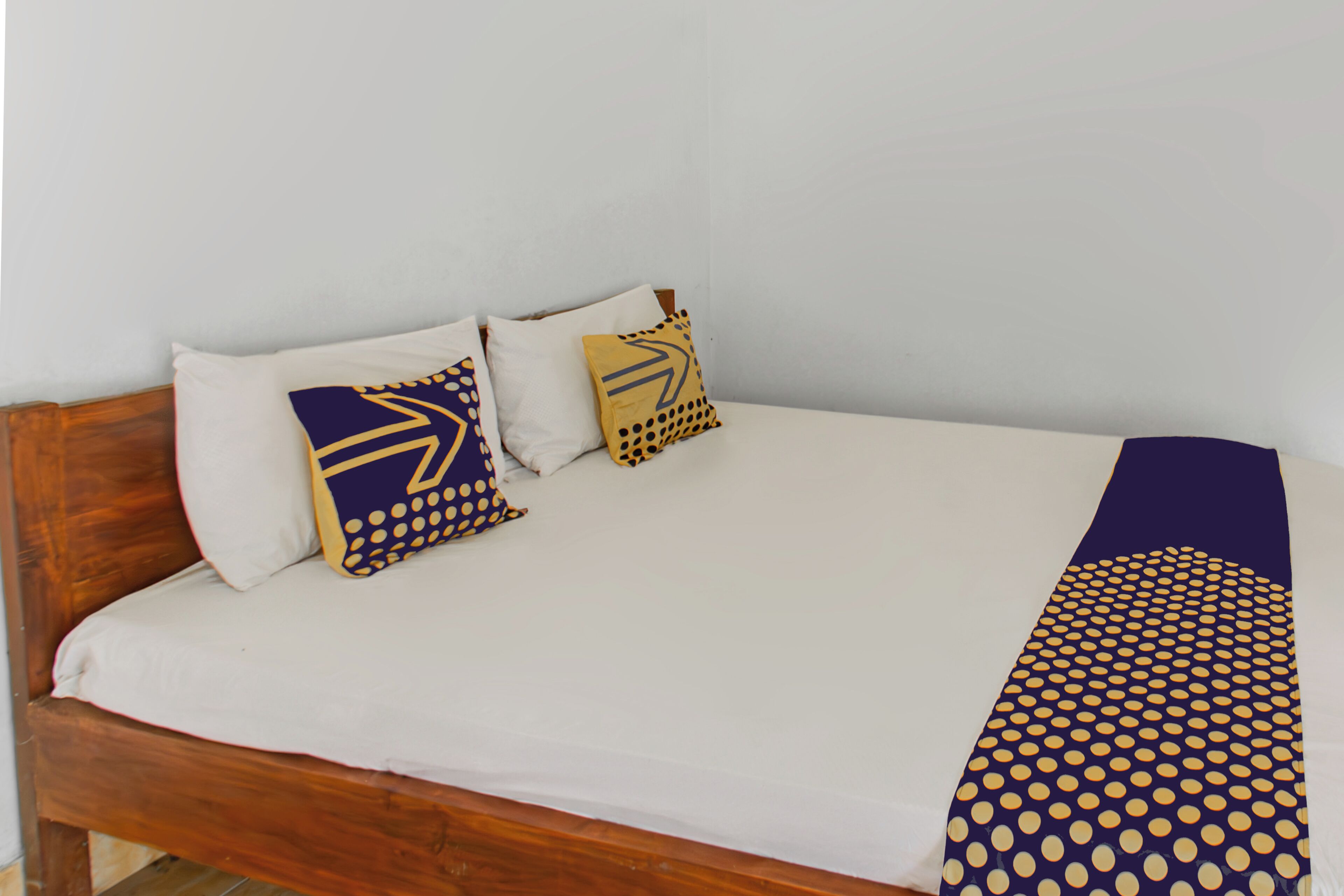 Una cama con cabecera de madera, ropa blanca de cama y dos almohadas decorativas con diseños geométricos.