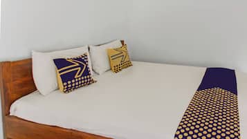 Una cama con cabecera de madera, ropa blanca de cama y dos almohadas decorativas con diseños geométricos.
