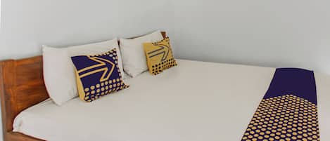Una cama con cabecera de madera, ropa blanca de cama y dos almohadas decorativas con diseños geométricos.
