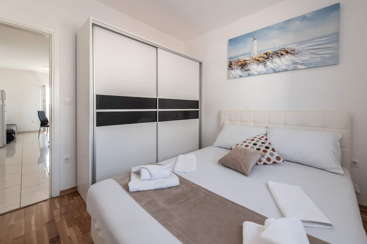 A hotel room with a bed, a wardrobe, a painting, and a view of the sea.