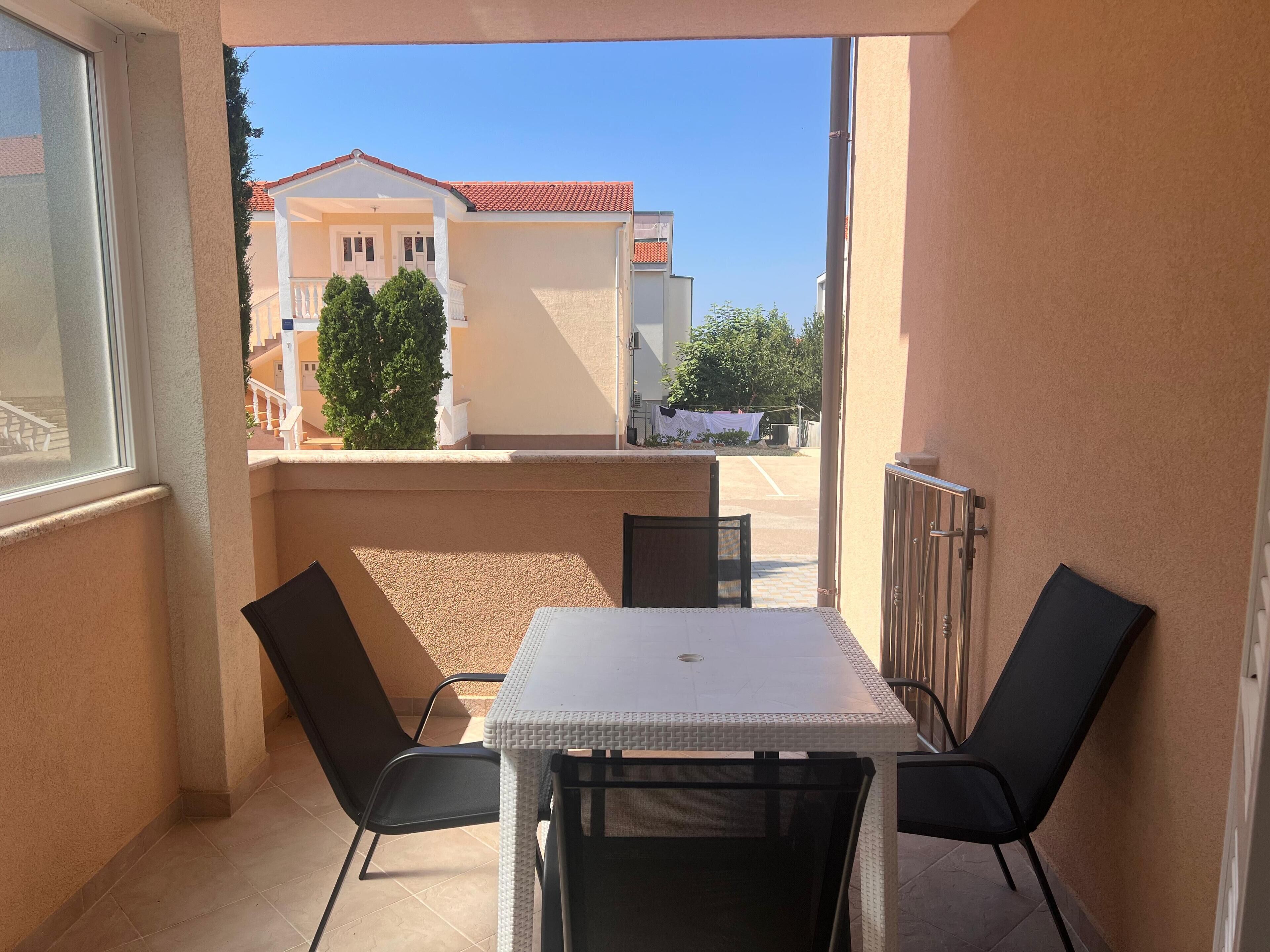 A balcony with a table and chairs, a view of neighboring buildings, and a clear sky.