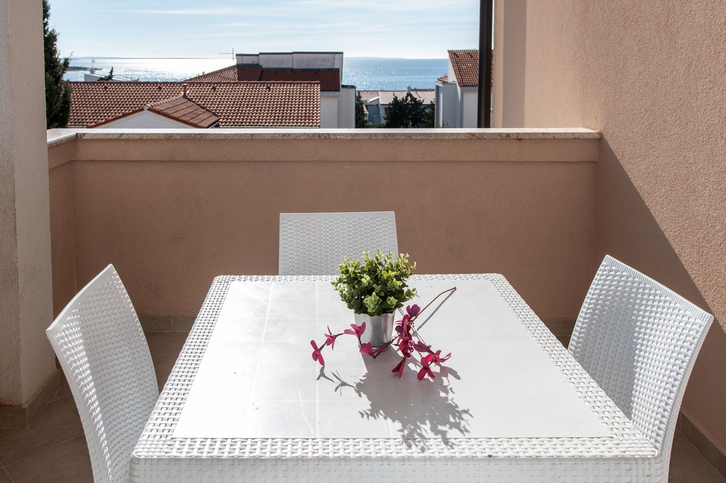 Et hvidt bord med stole på en balkon med udsigt til bygninger og havet.