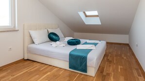Un dormitorio con techo inclinado, tragaluz, cama con ropa de cama blanca, almohadas turquesa y manta turquesa.