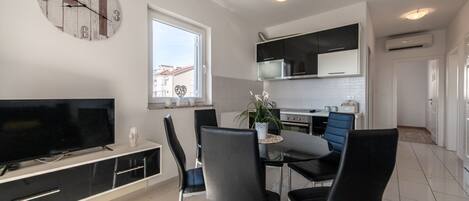 A modern kitchen with a dining area, a flat-screen TV, and a large clock on the wall.