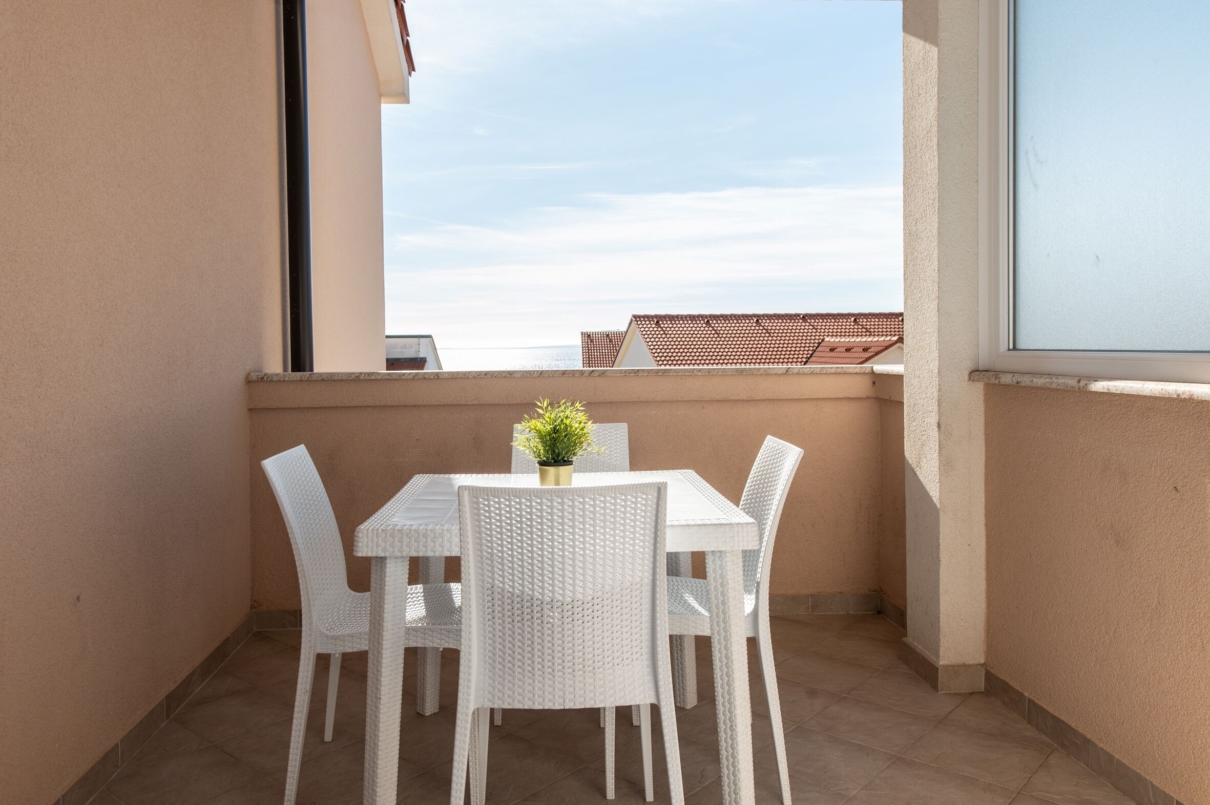 A balcony with a white table and chairs, a small potted plant, and a view of buildings and sky.