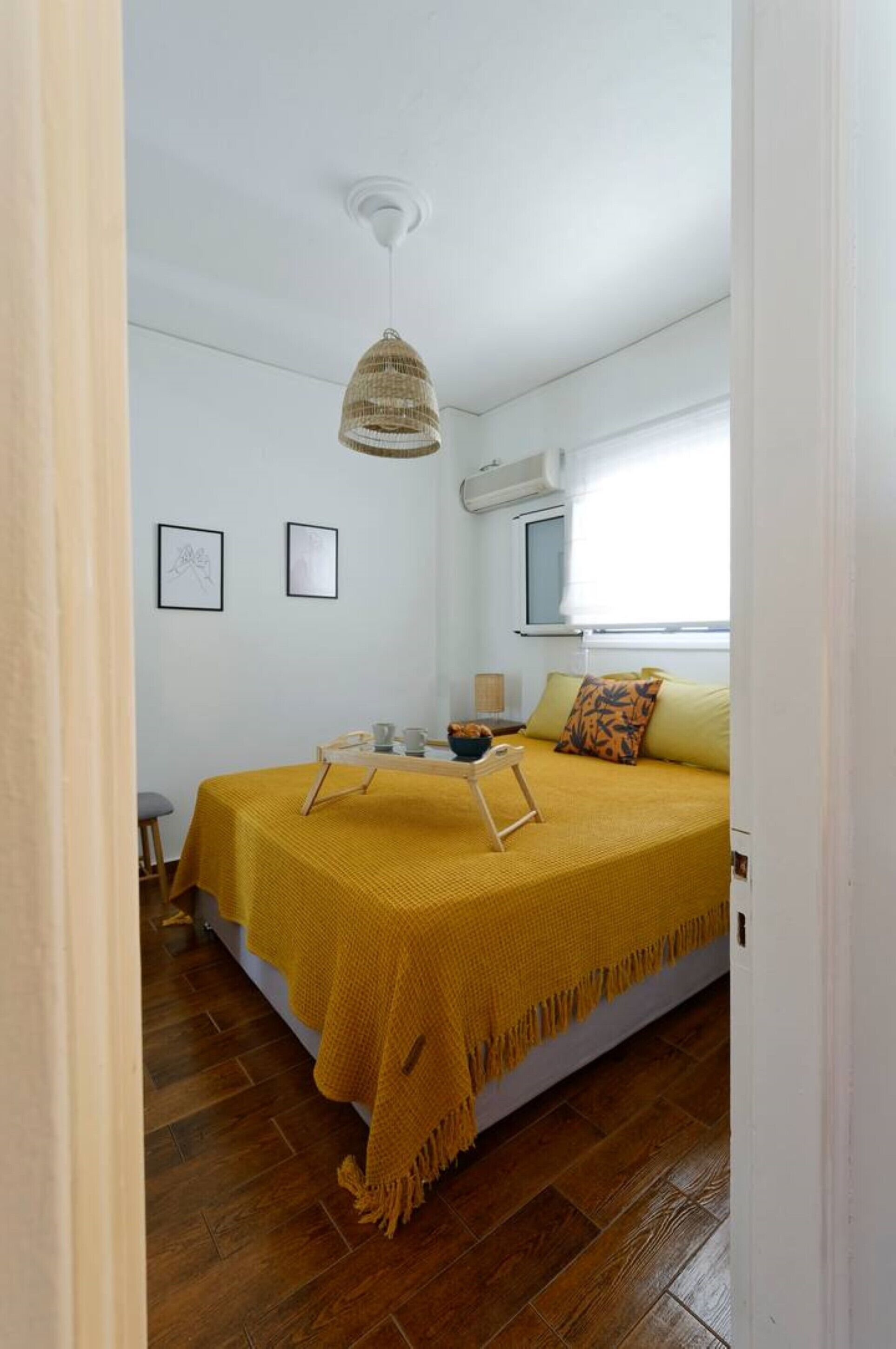 A bedroom with a bed, a hanging light fixture, a window, and a wall-mounted air conditioner.