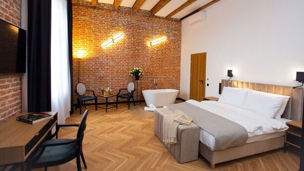 A modern bedroom with a brick wall, wooden beams, a large bed, a desk, and a chair. - Hotel Teatr  (Kraków)