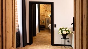 A hallway with wooden doors and a herringbone floor leading to a room with a stone wall and a bed. - Hotel Teatr  (Kraków)