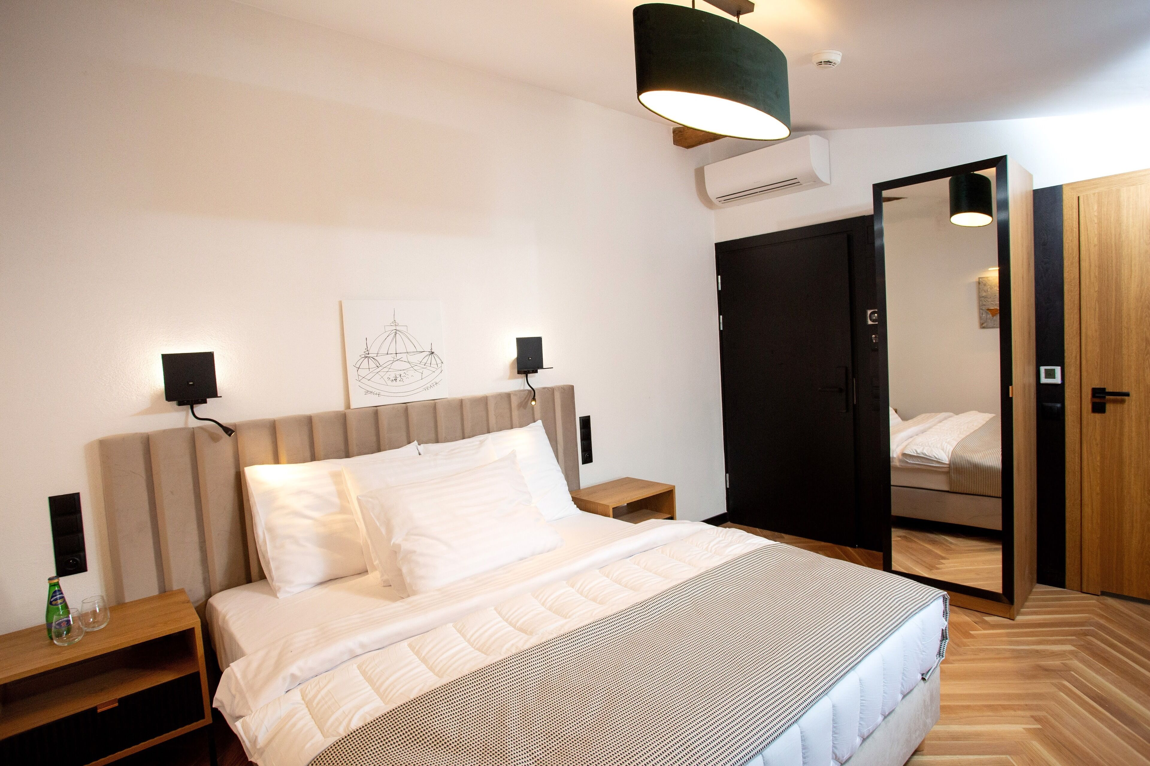 A modern bedroom with a large bed, bedside tables, a wall-mounted speaker, and a wardrobe with a mirror.