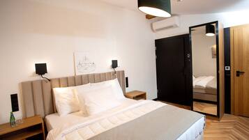 A modern bedroom with a large bed, bedside tables, a wall-mounted speaker, and a wardrobe with a mirror.