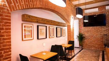 A restaurant interior with brick walls, wooden beams, framed certificates on the wall, and black chairs around wooden tables.