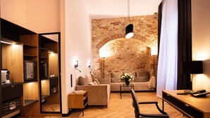 A modern hotel room with a wooden herringbone floor, a stone accent wall, a sofa, a coffee table, and a desk with a lamp. - Hotel Teatr  (Kraków)